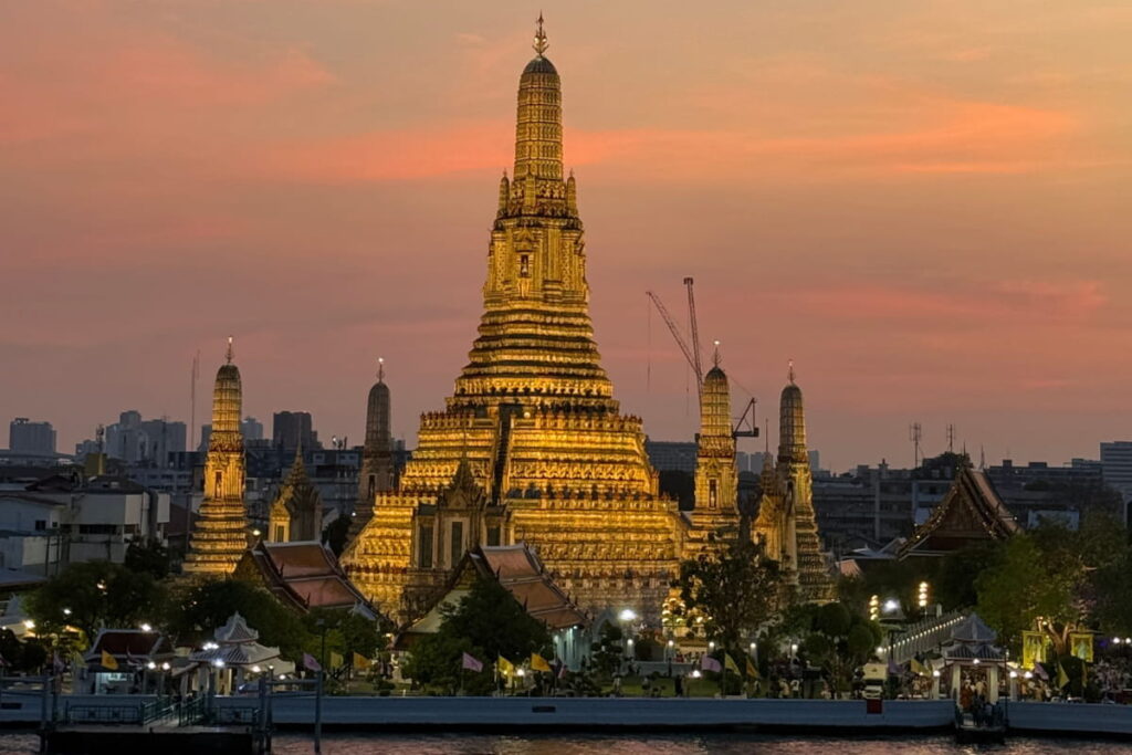 Wat Arun iluminado ao entardecer com céu alaranjado às margens do rio Chao Phraya, um belo ponto turístico de bangkok