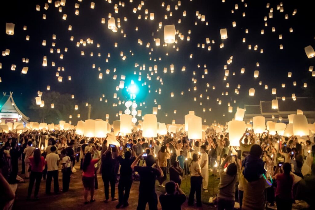 Multidão soltando lanternas de papel iluminadas no céu noturno durante o festival de lanternas em Chiang Mai, Tailândia